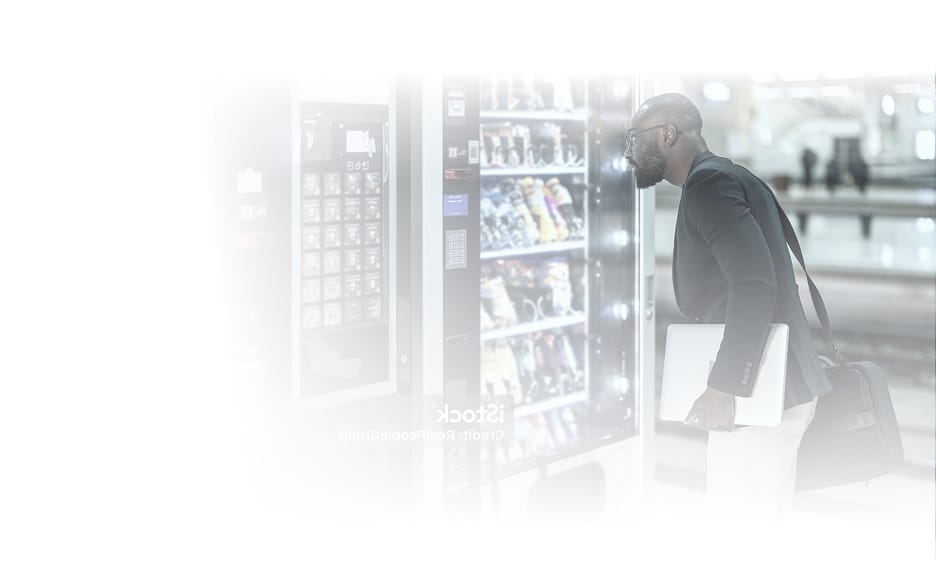 Man with a bag using a bank of snack and drink vending machines