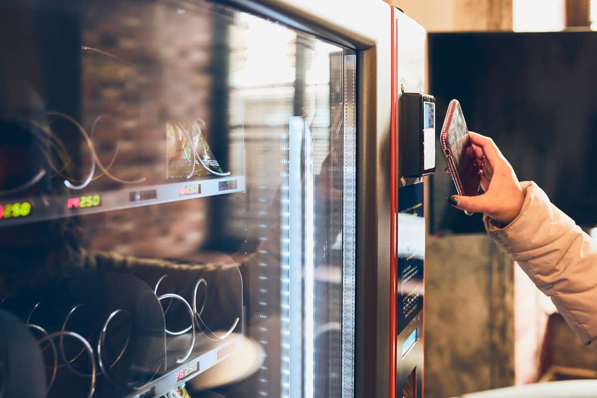 Hand holding a phone against the contactless payment reader on a vending machine