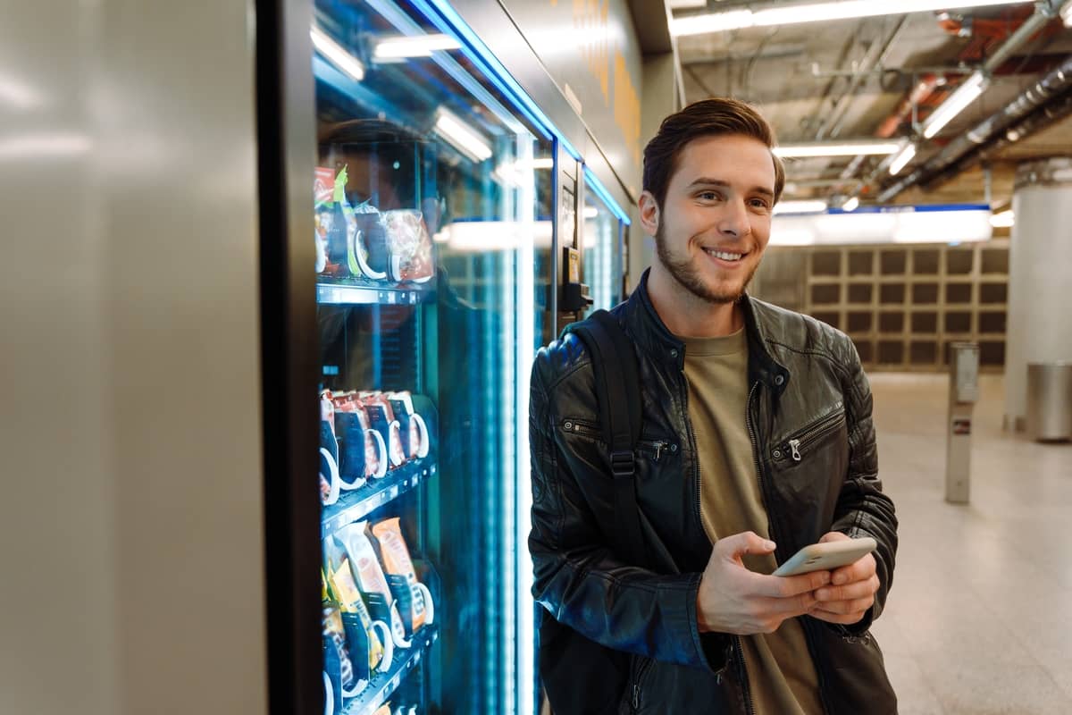 Smiling man holding a phone beside a refrigerated drinks cooler